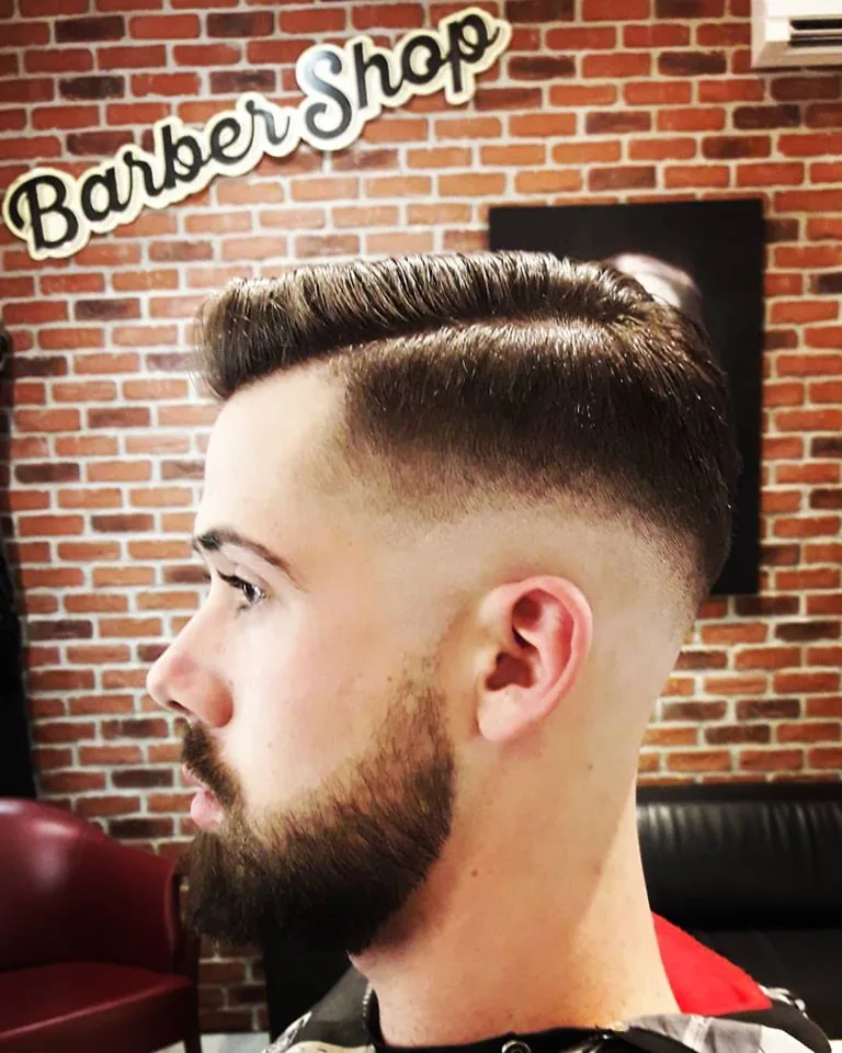 Dégradé et barbe taillée, devant le mur de briques du salon